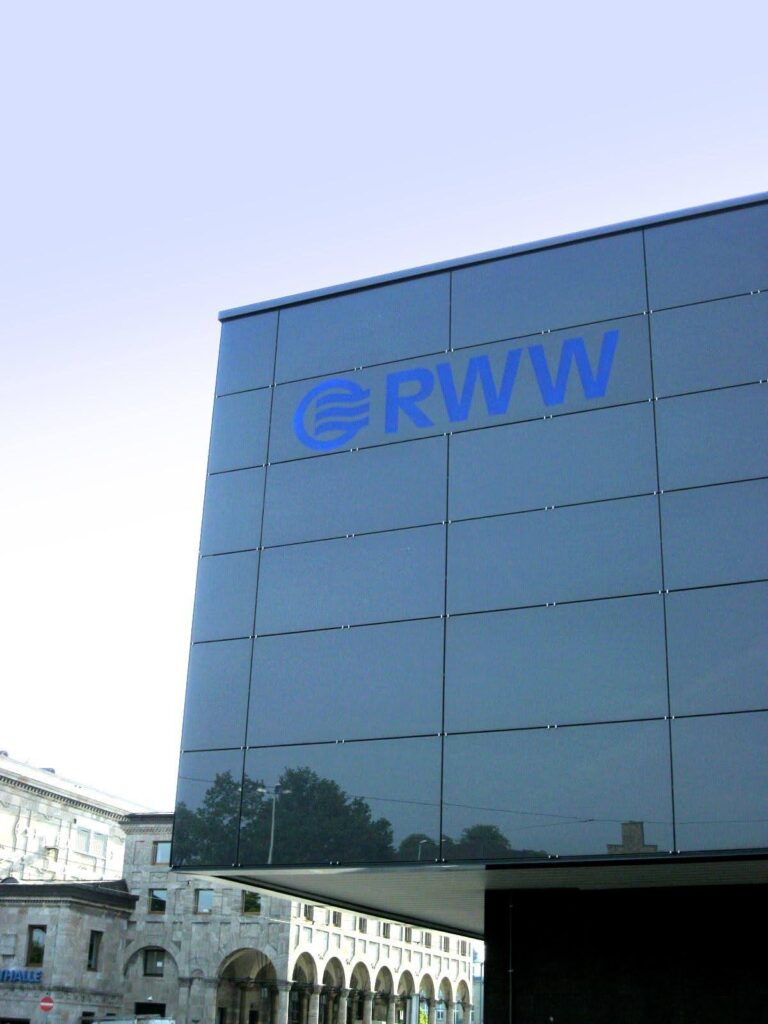 Verspiegelte Fassade und eingelassenes RWW LED-Logo, mit blauem Himmel im Hintergrund.