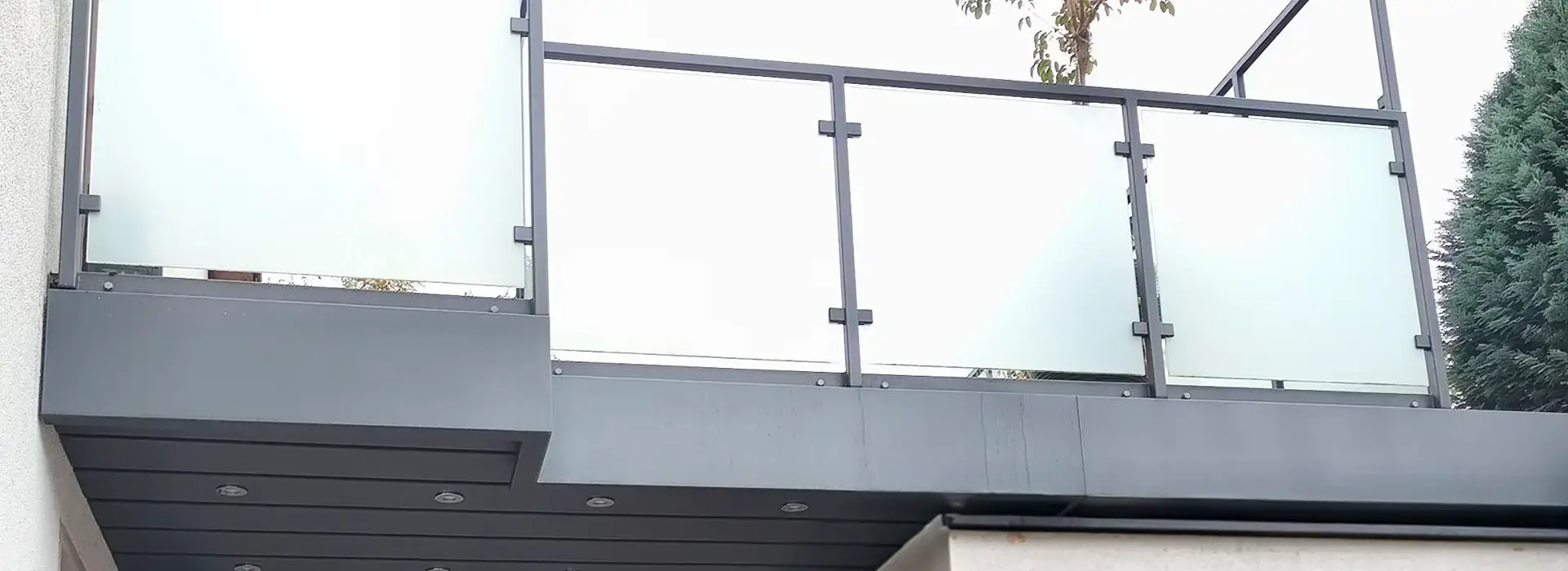 Ein modernes Haus mit zwei geschlossenen Garagentoren und einem Balkon darüber, mit Milchglasfenstern und Metallgeländer.