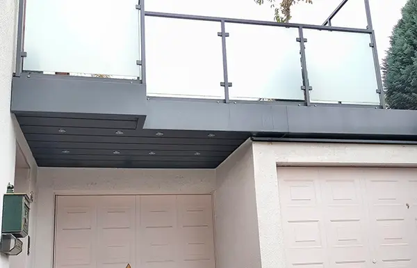 Ein modernes Haus mit zwei geschlossenen Garagentoren und einem Balkon darüber, mit Milchglasfenstern und Metallgeländer.